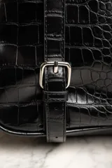 Mochila negra con textura símil cuero de cocodrilo, con dos compartimentos principales con cierre y asa de mano en la parte superior.