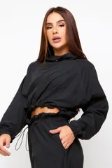Buzo cropped negro de estilo urbano, con cuello alto ajustable mediante cordón, mangas largas con puños elásticos y cintura con ajuste regulable.