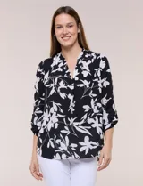 Blusa de gasa de calce suelto y caída ligera, color negro con estampado floral en blanco. Cuenta con cuello mao, escote en V, tabla central y mangas largas regulables con presilla y botón. El ruedo es redondeado y de estilo mullet, más largo en la parte posterior.