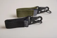 Llavero de cinta de poliéster color verde oliva con mosquetón y aro metálicos negros. Incluye etiqueta con el logo de la marca.