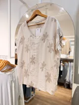 Blusa color beige de viscosa con escote en V y mangas cortas amplias. Presenta un diseño relajado con bordados florales en relieve distribuidos en toda la prenda.