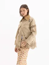 Chaqueta Sun de gabardina liviana color beige, de silueta recta con largo por debajo de la cadera. Presenta cuello de corderoy, detalles con apliques de encaje en mangas, hombros y ruedo, bolsillos frontales con solapa y cierre mediante broches metálicos.