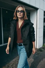Chaqueta acolchada de color negro con diseño de costuras onduladas, cuello subido y capucha ajustable. Cuenta con cierre frontal de cremallera oculto por una solapa con botones a presión, mangas largas y bolsillos laterales. Tejido con tecnología repelente al agua.