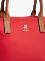Cartera tote Tommy Hilfiger de nailon rojo, con dos asas superiores en tono tostado y una correa de mano o hombro tejida extraíble. Cuenta con cierre de cremallera superior, compartimento principal e insignia metálica con el monograma TH en el frente.