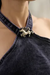 Top halter de denim con efecto lavado, corte entallado y escote alto. Presenta recortes frontales estructurados, terminación desflecada en el frente y un aplique metálico decorativo en el centro del cuello.