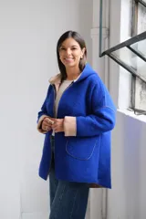 Tapado de paño color azul con capucha, cierre frontal y detalles en color beige en el interior de la capucha, puños y bordes de los bolsillos.