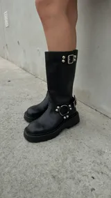 Botas de cuero negro de caña media con suela track, hebilla superior y arnés con tachas plateadas.