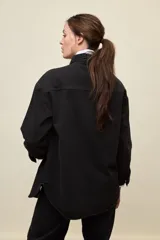 Sobrecamisa de denim de calce amplio y color azul, con cuello clásico, cierre frontal con broches metálicos y bolsillos delanteros con solapa.