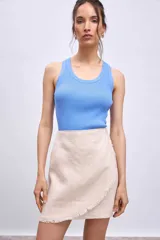 Minifalda color beige de corte evasé con diseño cruzado y detalle de flecos en el ruedo.