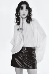 Pollera mini de corte ajustado confeccionada en tejido revestido con acabado desgastado efecto cuero. Presenta cintura clásica con cierre de botón, bolsillos decorativos con cierre en el frente y forro interior.