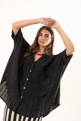 Camisa negra de corte oversize con diseño de encaje calado, escote en V, cierre frontal con botones y mangas tres cuartos. Presenta un diseño asimétrico con la parte posterior ligeramente más larga.