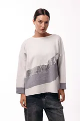 Sweater de punto con diseño de bloques de color en diagonal, combinando negro, beige y una franja central con textura metalizada. Presenta cuello redondo, mangas largas con puños en contraste y un corte holgado.