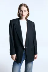 Blazer de corte oversize confeccionado en sarga, con hombreras marcadas, solapas clásicas y cierre frontal con un botón forrado a tono. Presenta dos bolsillos delanteros con solapa, logo bordado en una de las tapas y bordado decorativo en el cuello trasero. El diseño cuenta con un largo irregular que llega por debajo de la cadera y está completamente forrado.