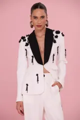 Blazer blanco con solapas negras de inspiración esmoquin, decorado con apliques florales y colgantes de cuentas negras bordados en el frente, hombros y mangas.