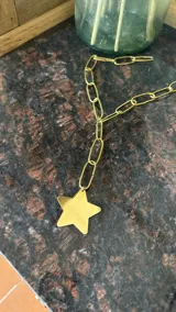 Collar de cadena de eslabones alargados en tono dorado con un dije colgante en forma de estrella de gran tamaño.