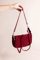 Cartera tipo bandolera de gamuza color negro, con cierre superior, tiras colgantes decorativas y herrajes metálicos plateados. Incluye asa corta para llevar al hombro y correa larga ajustable y desmontable.