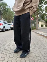 Pantalón tipo jogger de calce baggy, color negro, con una línea vertical blanca lateral y bolsillos laterales.