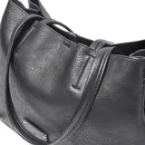 Cartera tipo tote de cuero sintético color negro, con doble asa de hombro, cierre superior y placa metálica decorativa con logo en el frente.