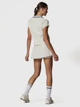 Polera de manga corta color blanco hueso, con cuello polo y abertura frontal en V. Presenta detalles de rayas finas en azul marino en el cuello y un pequeño logo bordado en el pecho.