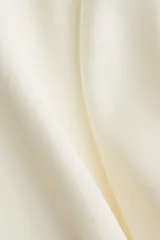 Blusa de manga globo larga color crema, con cuello redondo fruncido y botones ocultos en la parte delantera. Presenta un bajo redondeado.