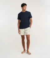 Bermuda de baño para hombre, color crema, con estampado repetitivo de peces azules. Presenta cintura elástica con cordón de ajuste y forro interior de malla.