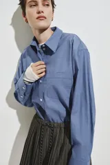 Camisa de corte oversized confeccionada en popelina de algodón con diseño de microcuadros. Presenta cuello clásico, bolsillo de parche en el pecho, cierre frontal con botones, hombros caídos y mangas largas con puños abotonados. Incluye canesú con pliegue en la espalda y bajo recto con aberturas laterales redondeadas.