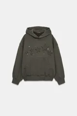 Sudadera con capucha y bolsillo tipo canguro, confeccionada en tejido con efecto lavado. Presenta diseño de estrellas bordadas y aplicación de tachas decorativas en el frente, con terminaciones en rib en puños y ruedo.