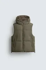 Chaleco puffer color verde militar, de corte regular fit, confeccionado en tejido técnico con acabado engomado. Cuenta con cuello subido, capucha ajustable, cierre frontal de cremallera, bolsillos laterales de vivo y bajo ajustable con cordón elástico.