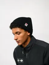 Gorro tipo beanie de punto acanalado en color negro, con vuelta y etiqueta de la marca Umbro cosida en el lateral.