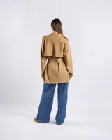 Campera tipo trench de color habano, de corte a la cadera, confeccionada en material textil símil gamuza. Presenta solapa cruzada, doble botonadura frontal, hombreras y cinturón ajustable para anudar en la cintura. Incluye bolsillos delanteros y puños con trabilla.