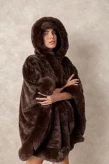 Capa de piel sintética en color negro, con diseño holgado, capucha integrada y bordes con textura de pelo largo.