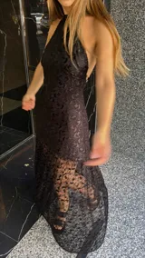 Vestido largo de encaje negro con cuello halter y espalda descubierta. Tiene un corte a la altura de la rodilla y un ruedo largo transparente.