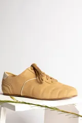 Zapatillas bajas color crema con cordones y suela marrón.