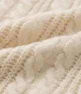 Suéter de punto pesado color crema, con cuello redondo y mangas largas. Presenta textura trenzada.