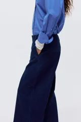 Pantalón de jean tipo wide leg de tiro alto, confeccionado en denim rígido de color azul oscuro. Presenta un corte holgado desde el muslo hasta el ruedo, con raya marcada en el centro de las piernas, cierre con botón oculto y bolsillos al bies.