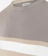 Suéter de punto con cuello redondo y manga larga, diseñado con un patrón de bloques de color en tonos beige, blanco y gris. Presenta un corte regular que se ajusta de forma anatómica al cuerpo.