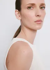 Vestido corto blanco sin mangas, con cuello redondo y detalle de lazo lateral en la cintura.