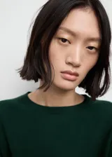 Vestido corto de punto fino, color verde oscuro, con cuello redondo y mangas largas. Presenta un diseño recto y minimalista.