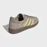 Championes Adidas modelo Handball Spezial, confeccionados en gamuza color marrón con las icónicas tres rayas laterales y detalles en color verde lima. Presentan suela de caucho color caramelo y el logo Spezial en el lateral.