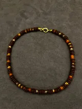 Collar corto de piedras volcánicas negras en la base del cuello, con pequeños detalles en tonos tostados y dorados.