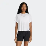 Remera deportiva de mujer New Balance, de corte holgado y largo cropped, con mangas cortas y escote redondo. Presenta aberturas laterales para mayor movilidad y el logo de la marca estampado en el centro del pecho.