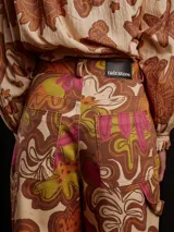 Pantalón de gabardina color marrón con estampado floral, corte carrot fit, tiro medio, estilo carpintero y detalles de botón de metal personalizado y parche trasero personalizado.