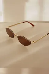 Lentes de sol con montura metálica dorada y cristales de forma geométrica (diamante/hexagonal) en tono marrón. Las patillas son doradas con puntas negras.