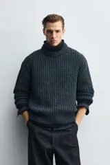 Jersey de punto grueso con estructura de volumen, corte relajado, cuello redondo y manga larga con puños y ruedo acanalados. Presenta un diseño bicolor con trama en tonos verde oscuro y azul.
