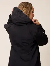Campera de corte recto y estilo funcional, color beige, con capucha integrada, cierre frontal con botones a presión y bolsillos delanteros amplios. Presenta un diseño minimalista con cordones ajustables en la capucha.