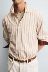 Camisa de corte relajado confeccionada en tejido con mezcla de viscosa, con diseño de rayas verticales en tonos beige y marrón. Presenta cuello solapa, cierre frontal de botones, manga larga con puños abotonados y un bolsillo en el pecho.