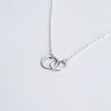 Collar de cadena fina con dije compuesto por dos argollas entrelazadas de plata 925 con acabado pulido.