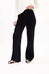 Pantalón de punto negro de corte recto y tiro alto, con cintura elástica ajustable mediante cordón y detalle de costuras verticales con flecos a lo largo de las piernas.
