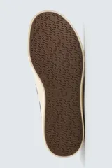 Zapatilla tipo slip-on de lona color taupe, con elástico lateral para facilitar el calce y suela de goma gruesa color crema.