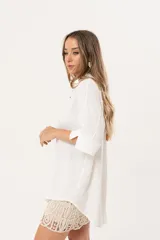 Camisa blanca de silueta oversize, con cuello camisero, manga 3/4 y corte más largo en la espalda. Presenta bordados de coral y caracol en el frente, y botones a tono.